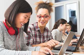 [Featured Image] Two students earning a computer science degree are sitting together and studying while looking at their computers.