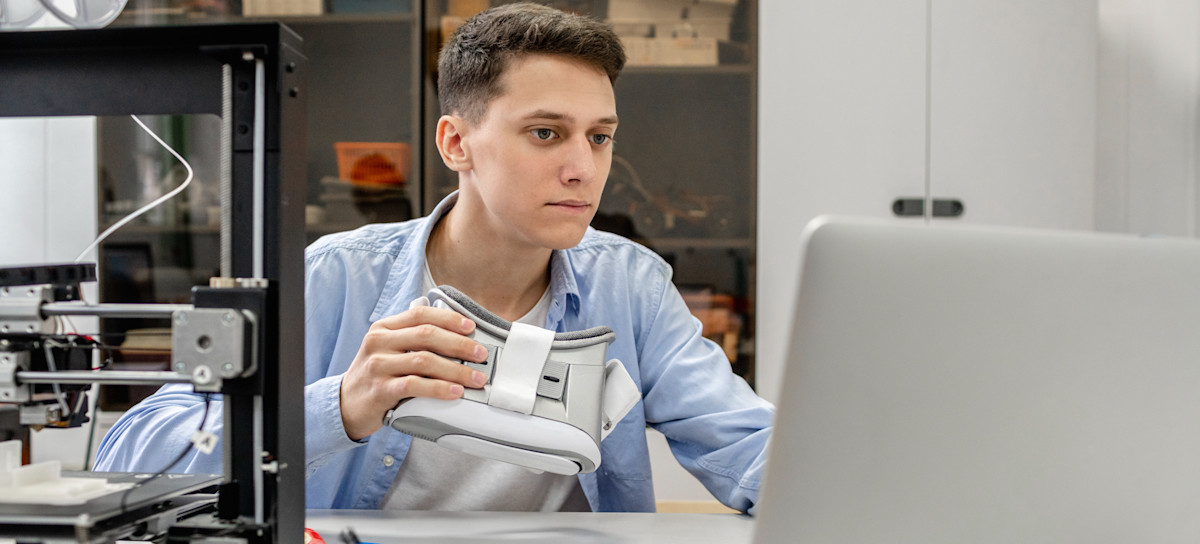 [Featured Image] A game tester in a blue shirt holds a VR headset and reviews information on their laptop.