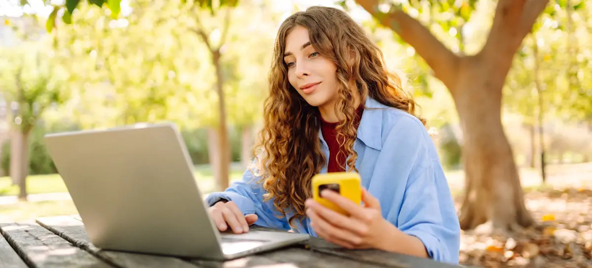 [Featured Image] A social media specialist sits outdoors with a laptop and phone, helping to create marketing content.
