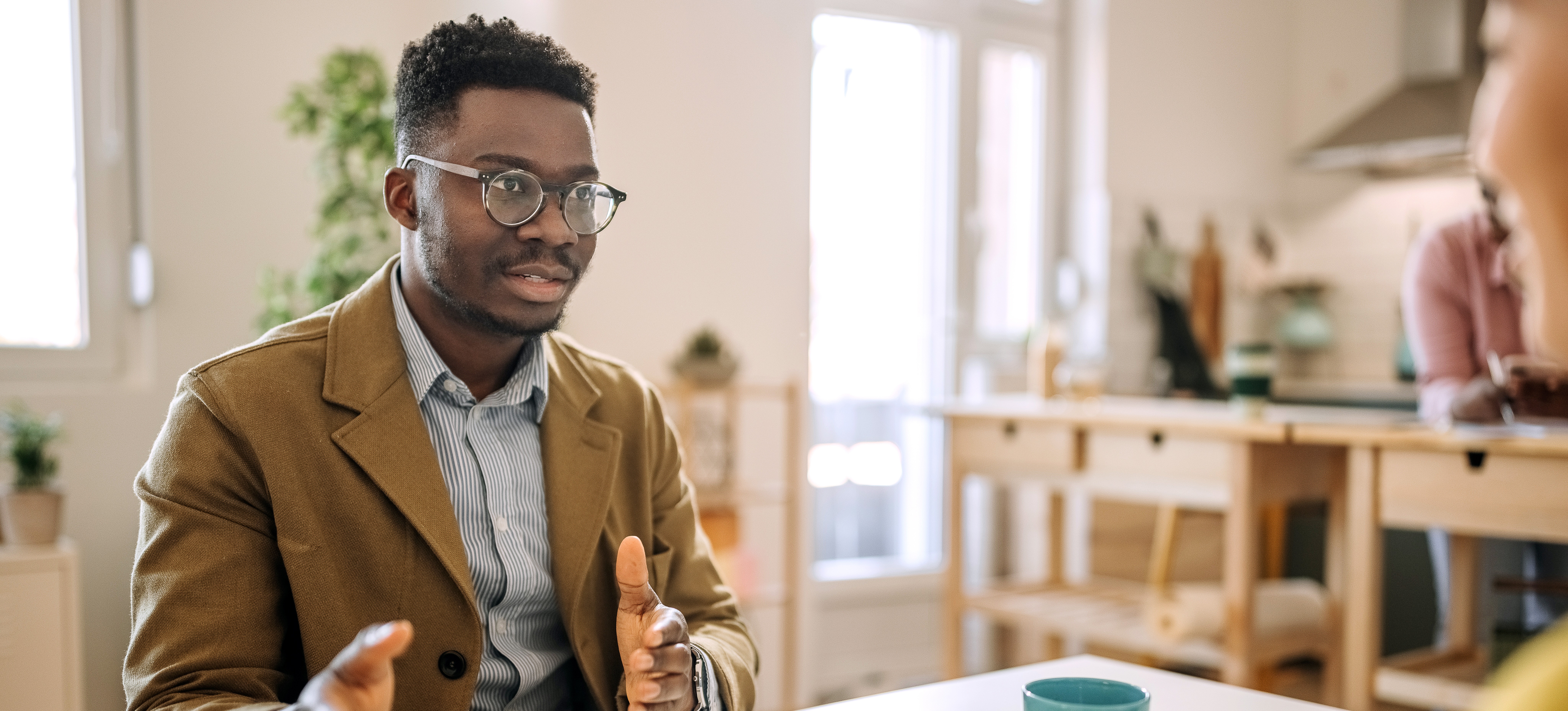 [Featured Image] A person wearing glasses and a blazer sits across a table from an HR representative and answers GAN interview questions.
