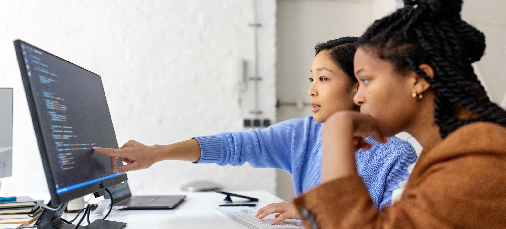 [Featured Image] An SQL specialist teaches a professional in a work environment, discussing ways to improve SQL skills.
