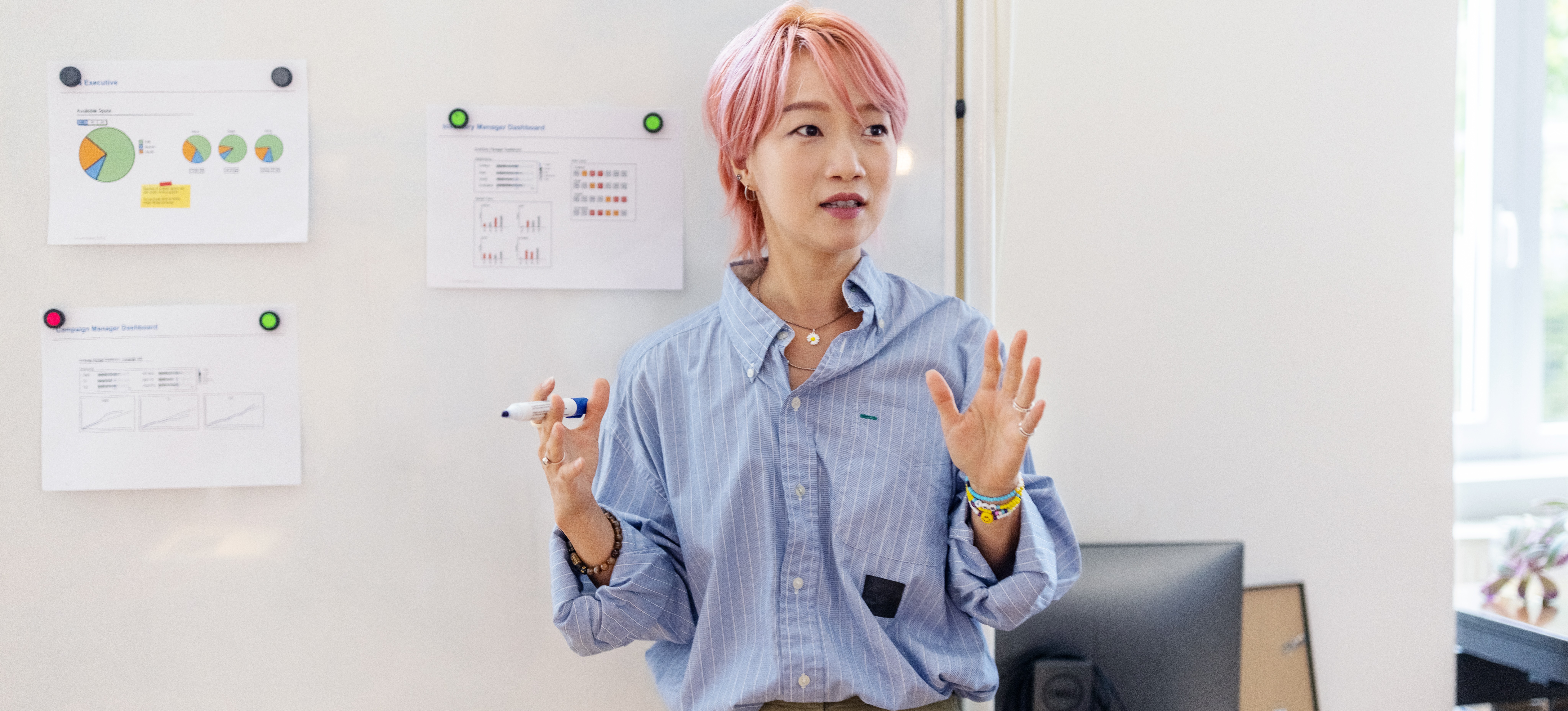 [Featured Image] Person explaining data lineage to an unseen team at the office. The person stands by a whiteboard with statistical graphs, giving a presentation to an unseen audience.
