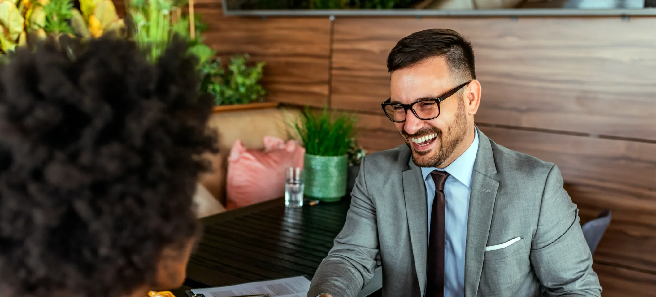 [Featured image] A human resources business partner is sitting at their desk talking to their coworker. 