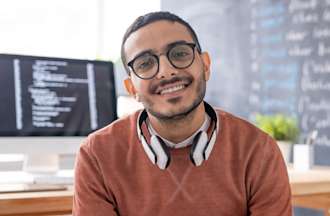 [Featured image] A data scientist in a coral sweater and glasses sits in front of a computer with programming language on the screen.