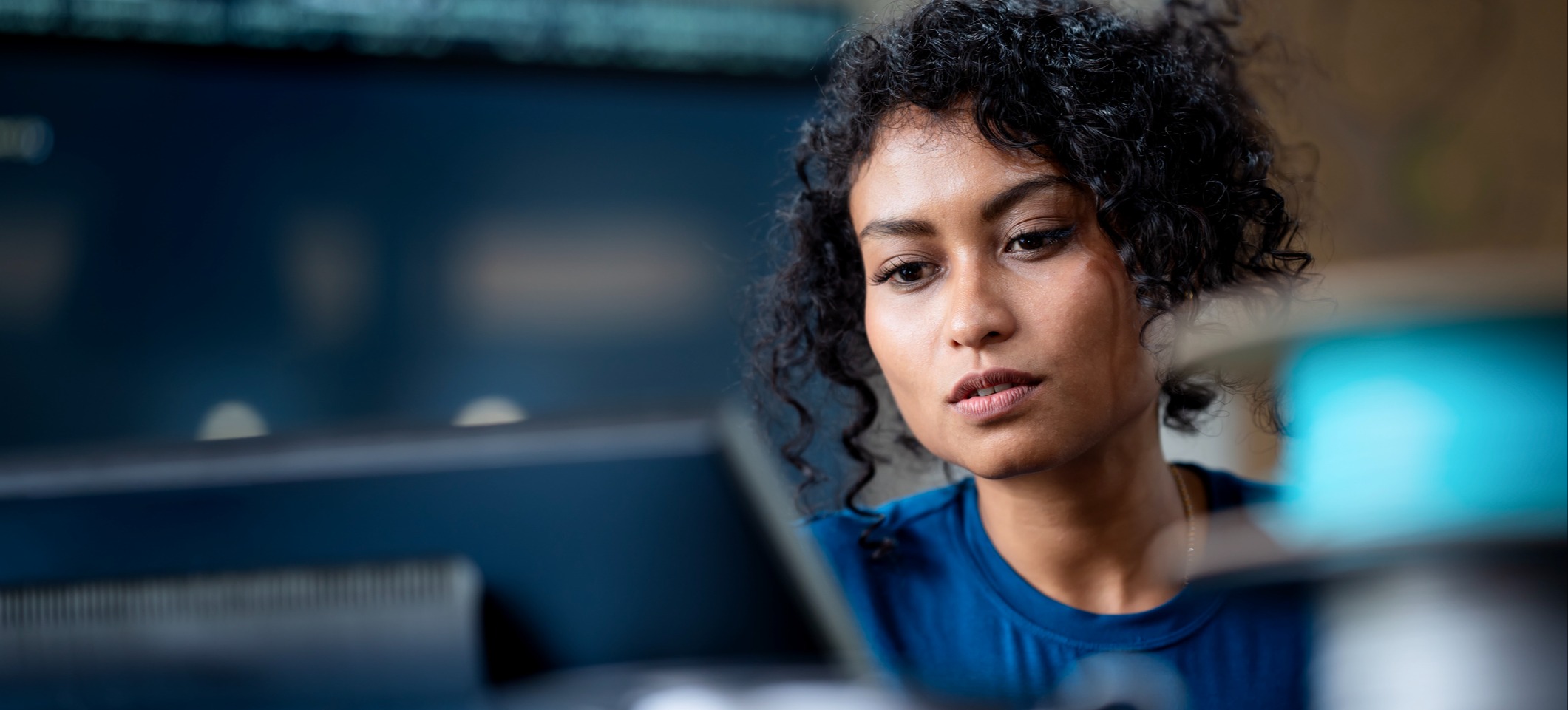 [Image en vedette] Une femme concentrée travaille sur un ordinateur de bureau dans une pièce sombre, son visage éclairé, en train d'apprendre ce qu'est le deep learning.