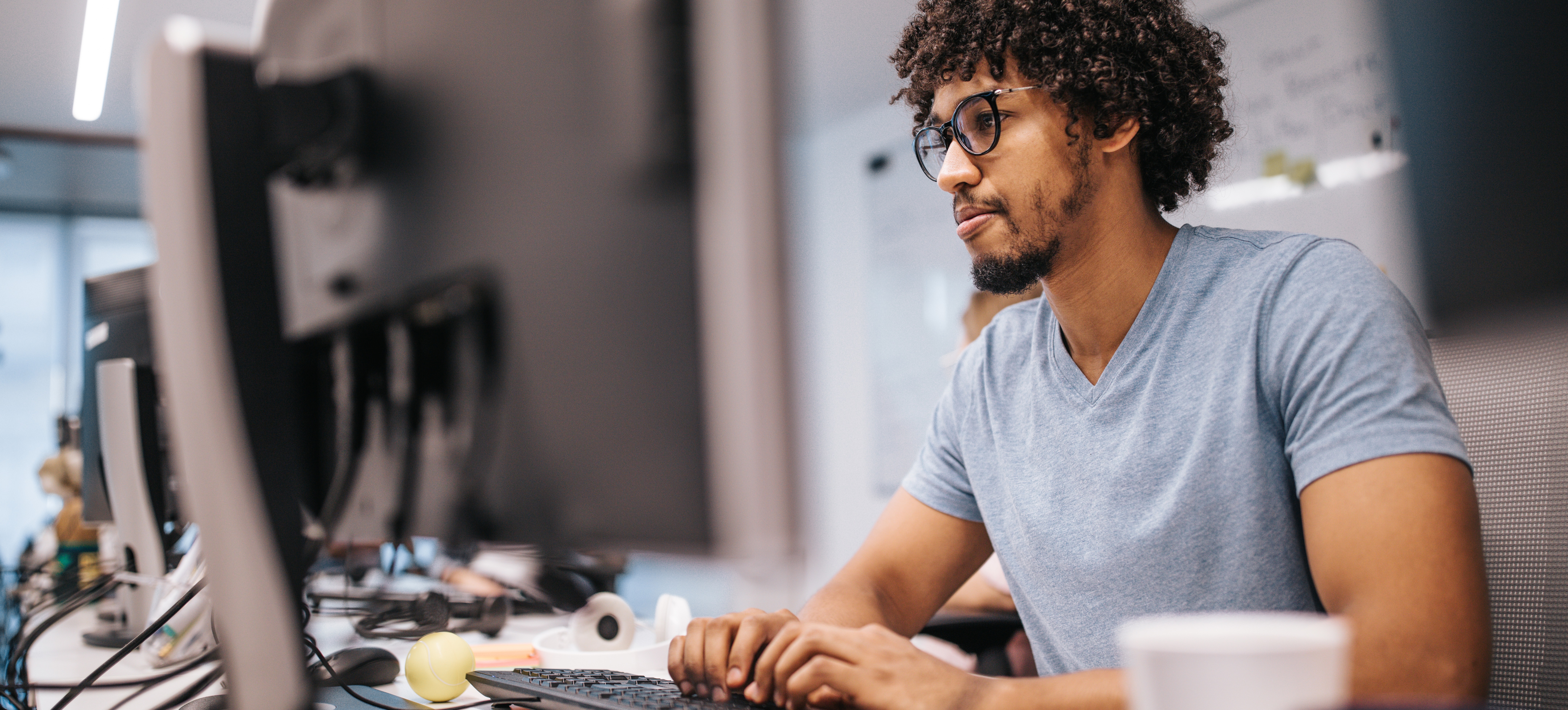 [Featured Image] A male data engineer is wearing a blue shirt and working at his computer in an office setting.