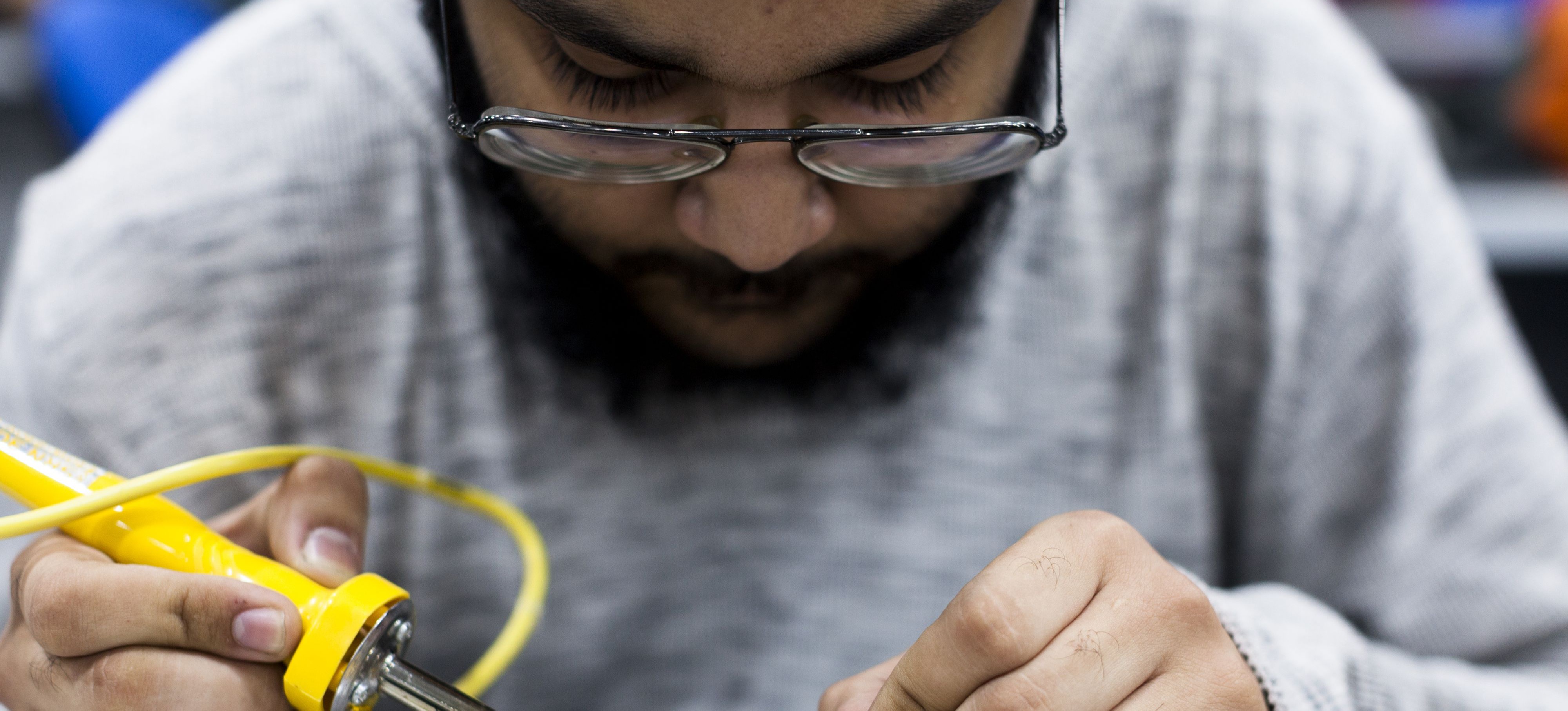 [Featured Image]: A team member solders a part on a computer chip as he works on a step in the product management process.
