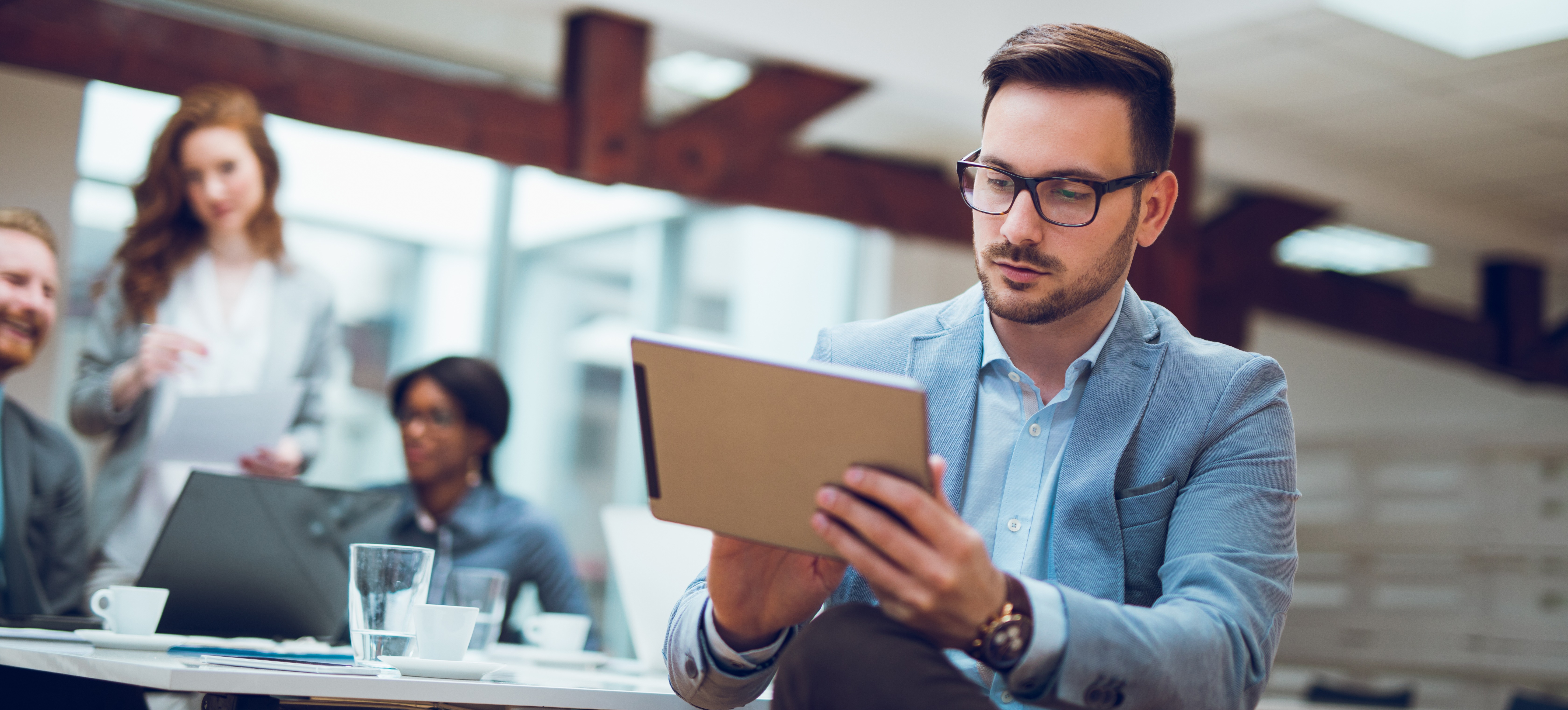 [Image en vedette] Personne travaillant sur une tablette pendant que des collègues discutent. 