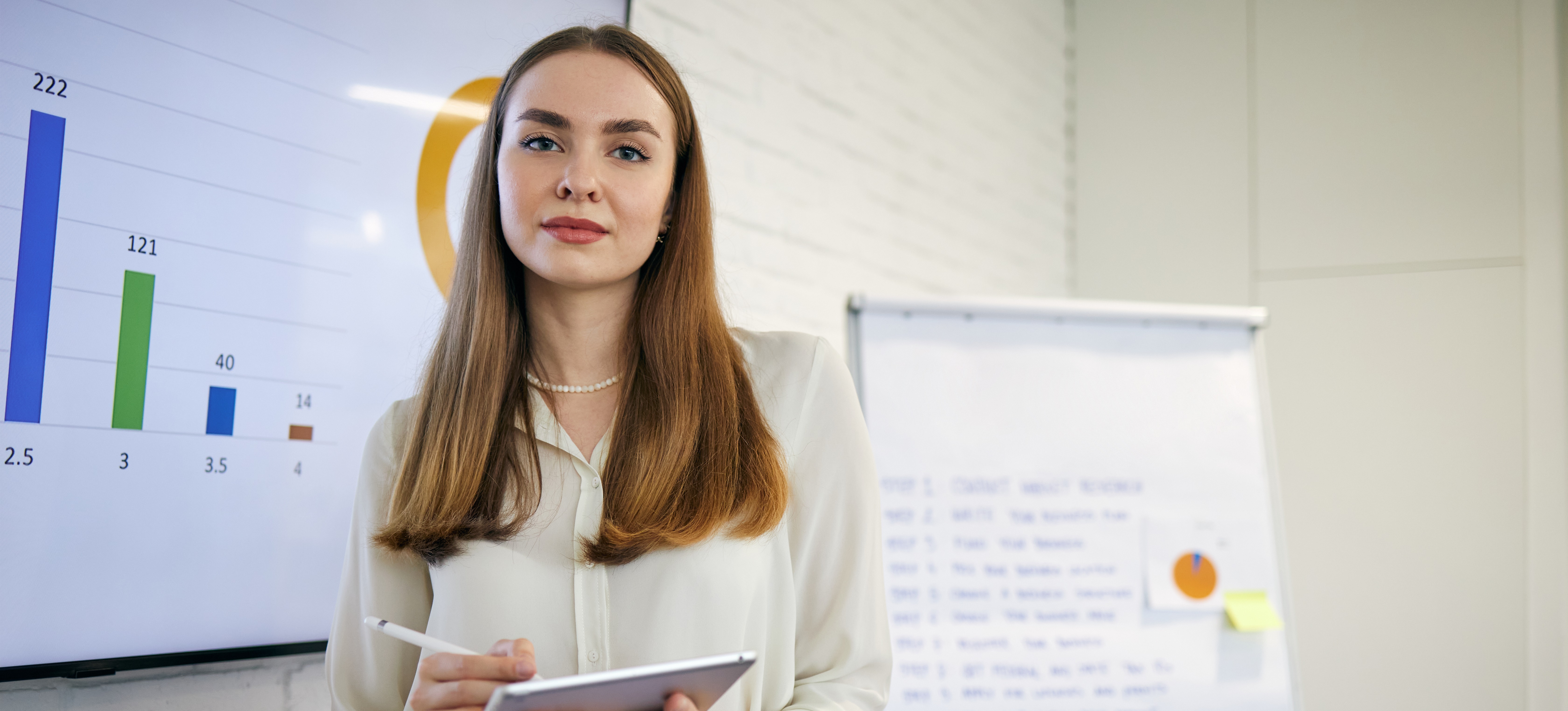 [Featured image] Woman in front of whiteboard and easel holding a development plan on a tablet.