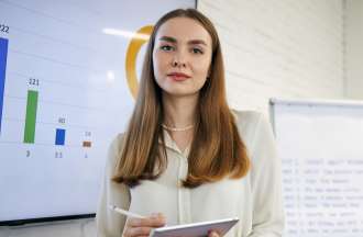 [Featured image] Woman in front of whiteboard and easel holding a development plan on a tablet.