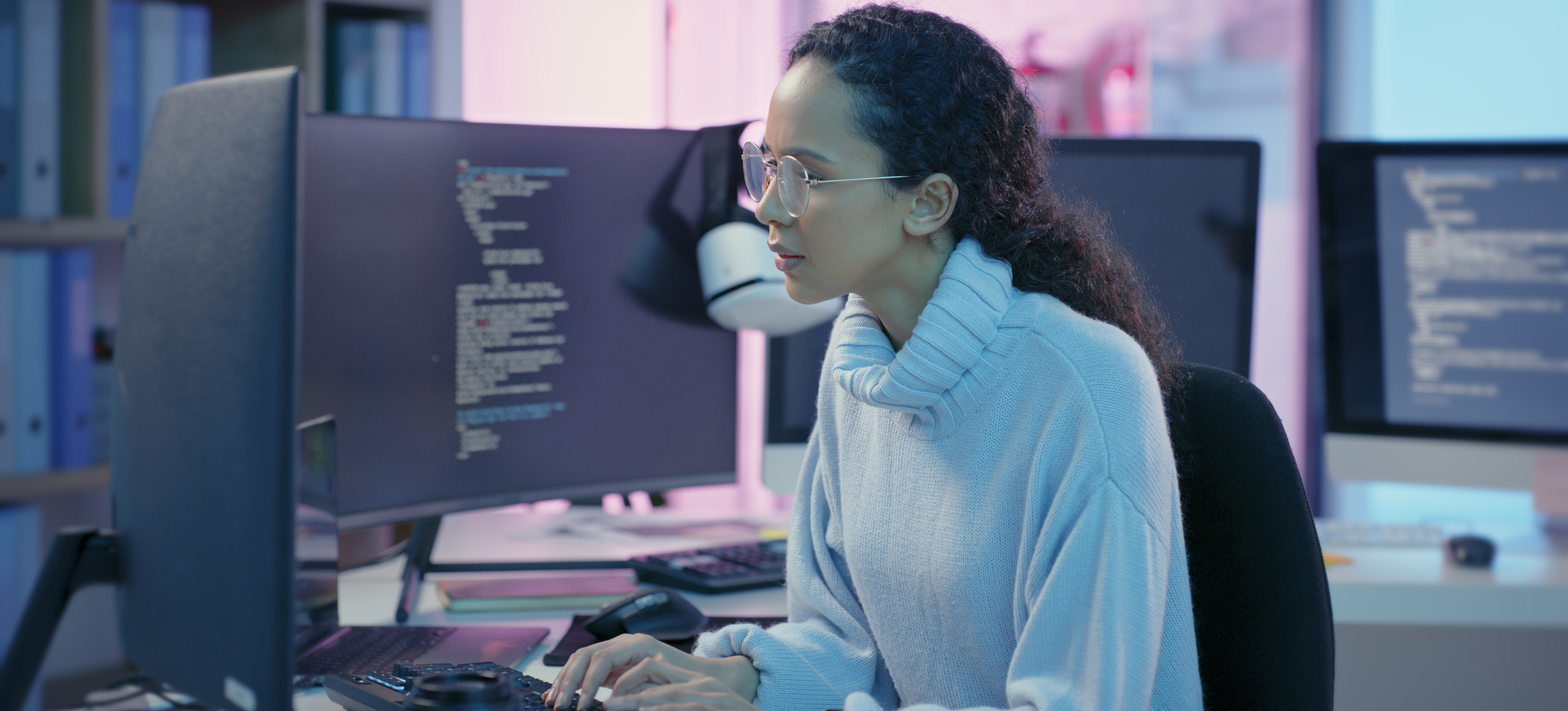 [Hauptbild] Eine Frau, die für ein CISSP-Gehalt arbeitet, sitzt an einem großen Schreibtisch mit mehreren Desktops und tippt auf einer Tastatur.