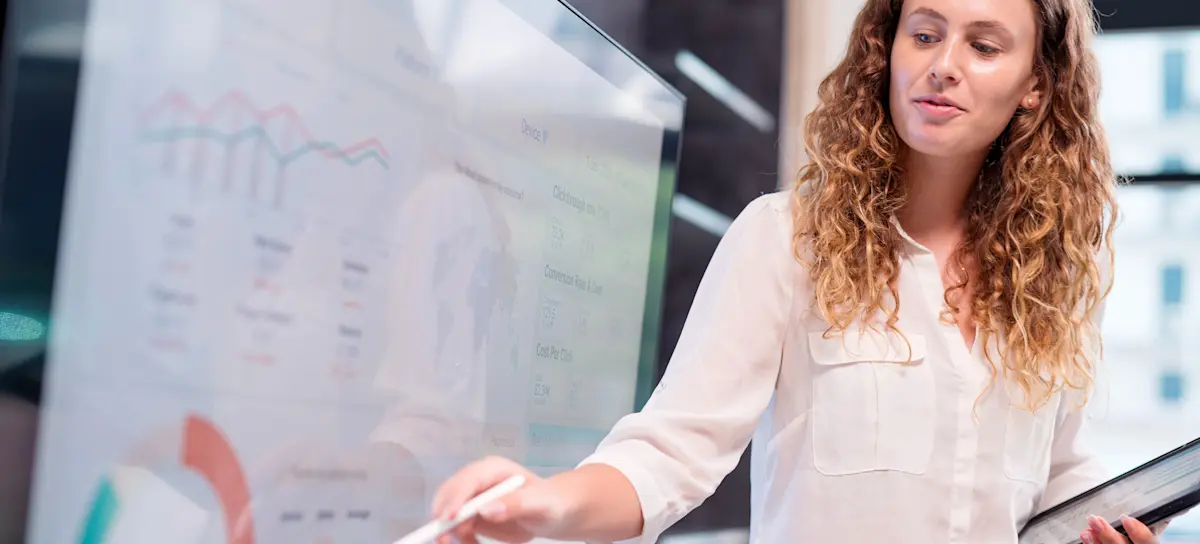 [Featured Image] After attending a data analytics boot camp, a data analyst feels more confident as they present to their colleagues, pointing to a screen filled with graphs and charts.
