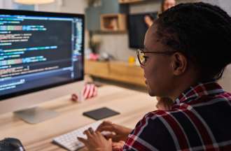 [Featured image] A person wearing glasses and a plaid shirt works on code on a desktop.