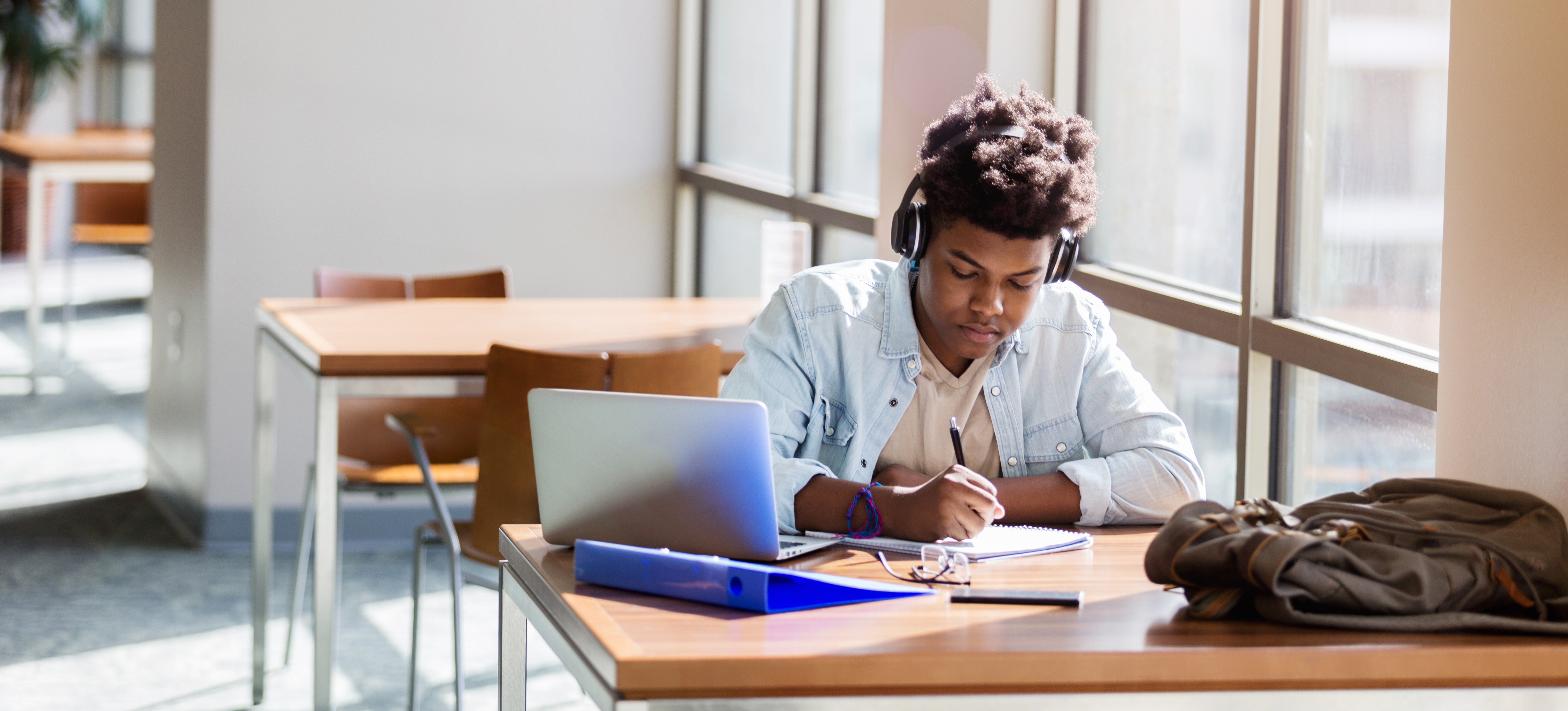 [Featured Image] A high school student sits in a library working on their responses to the Common App essay prompts.
