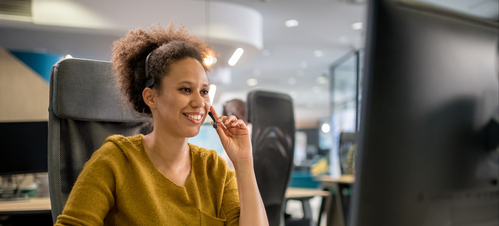 [Featured image] A customer service agent sits at their desk in front of a desktop computer, talking to a customer.