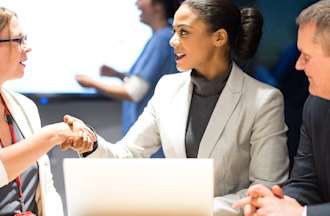 [Featured Image] A professional meets and shakes hands with potential customers as part of her cybersecurity sales job.