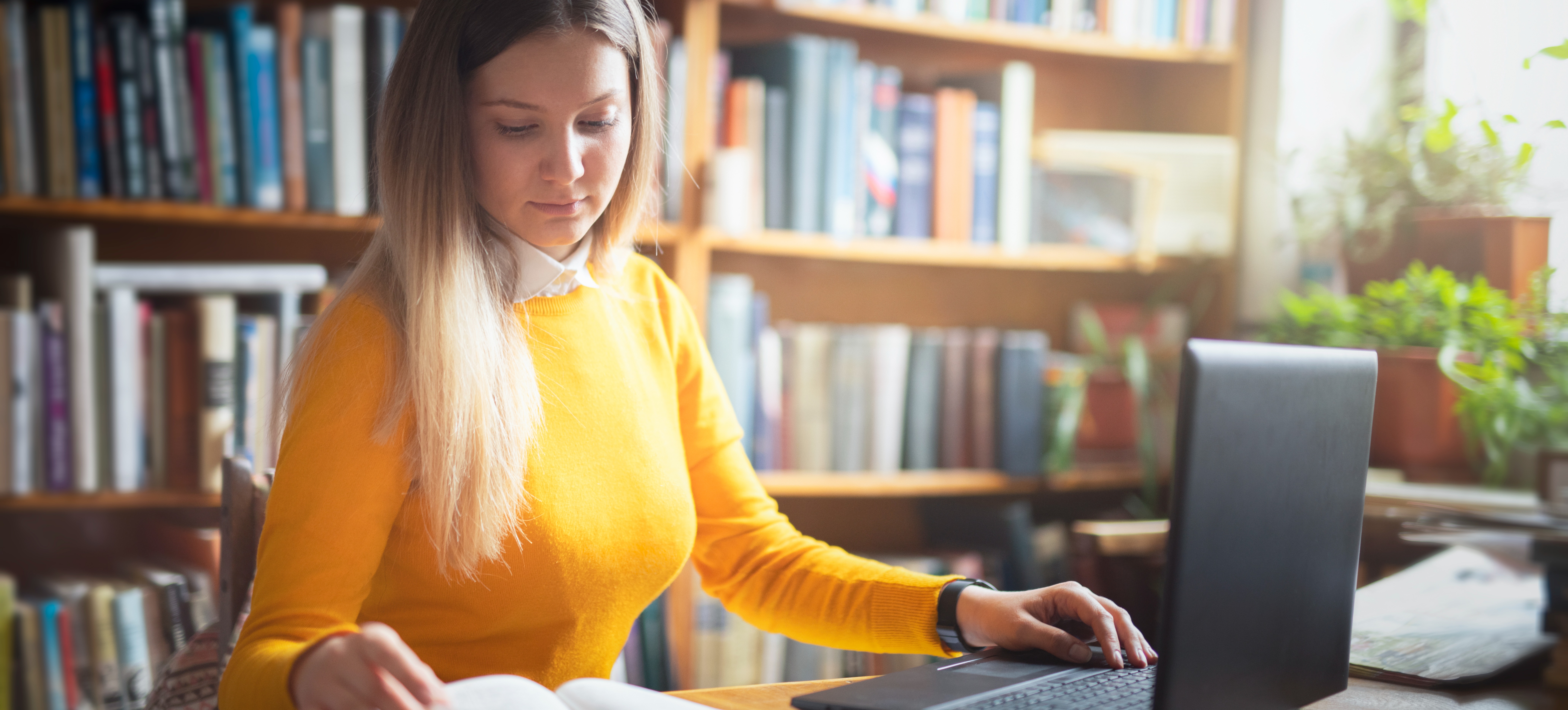 [Featured Image] A student studies in a library, preparing for a business degree.