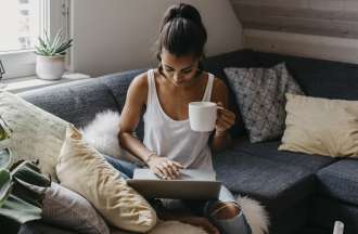 [Featured image] A woman sits on a couch, holding a white mug, as she types a data analyst cover letter on her laptop.