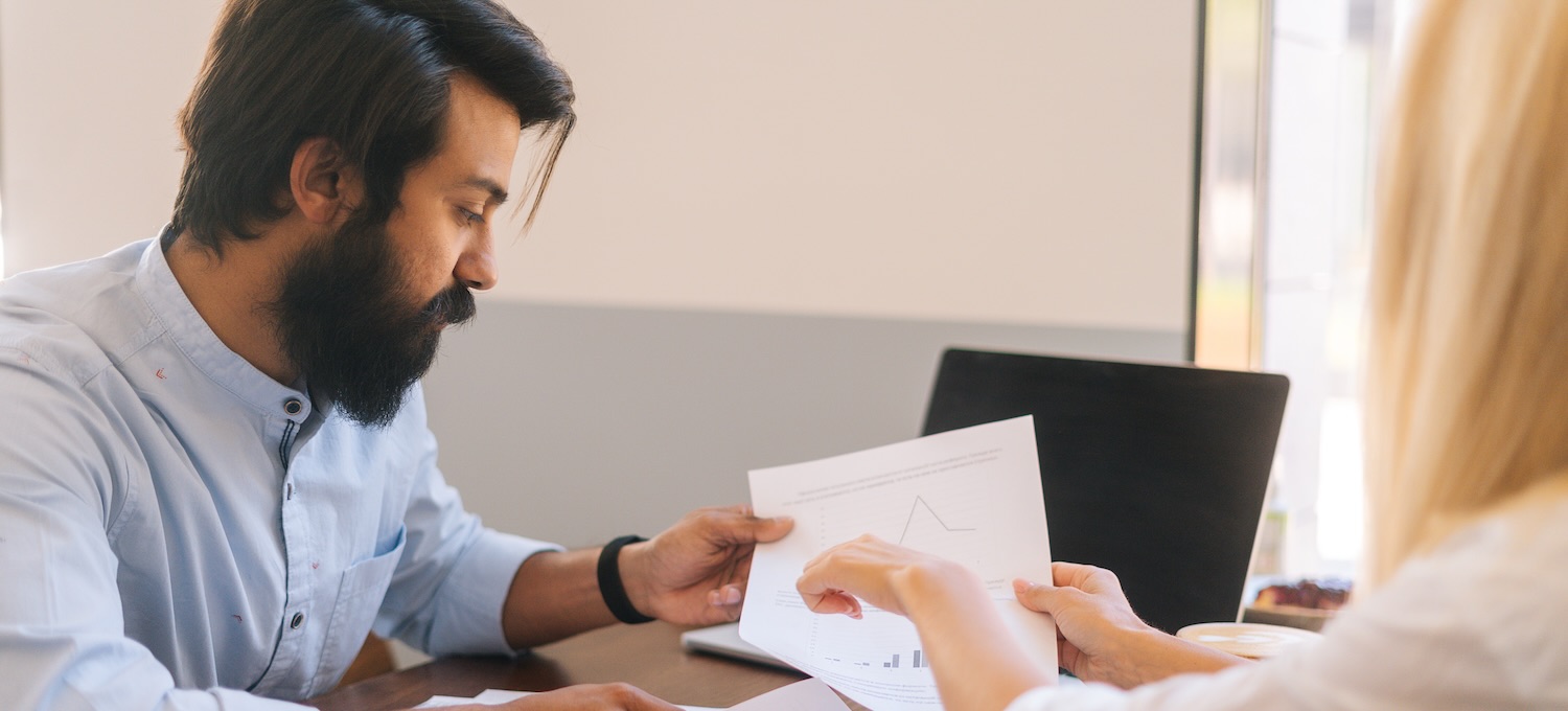 [Featured Image] Two human resources colleagues discuss converting hourly to salary as they determine the proper pay structure for their employees. 
