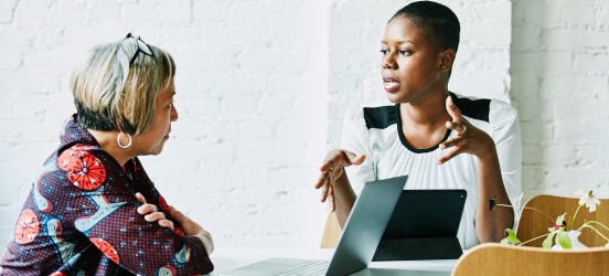[Featured image] One person speaks while the other listens, with a laptop in the foreground.
