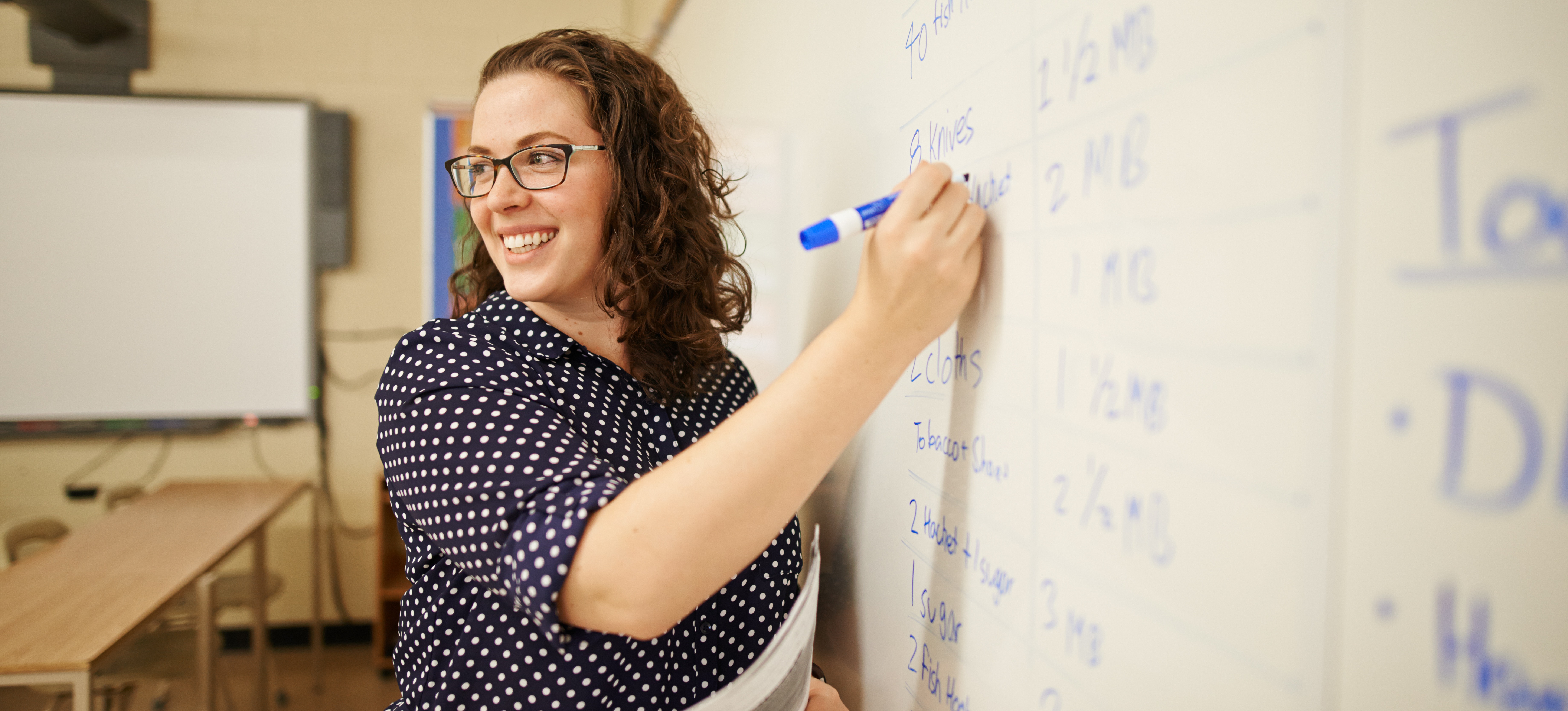 [Featured Image] A teacher writes on the whiteboard in their classroom after earning their degree.