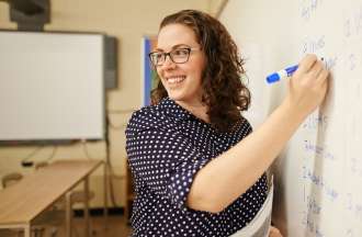 [Featured Image] A teacher writes on the whiteboard in her classroom after earning her degree.