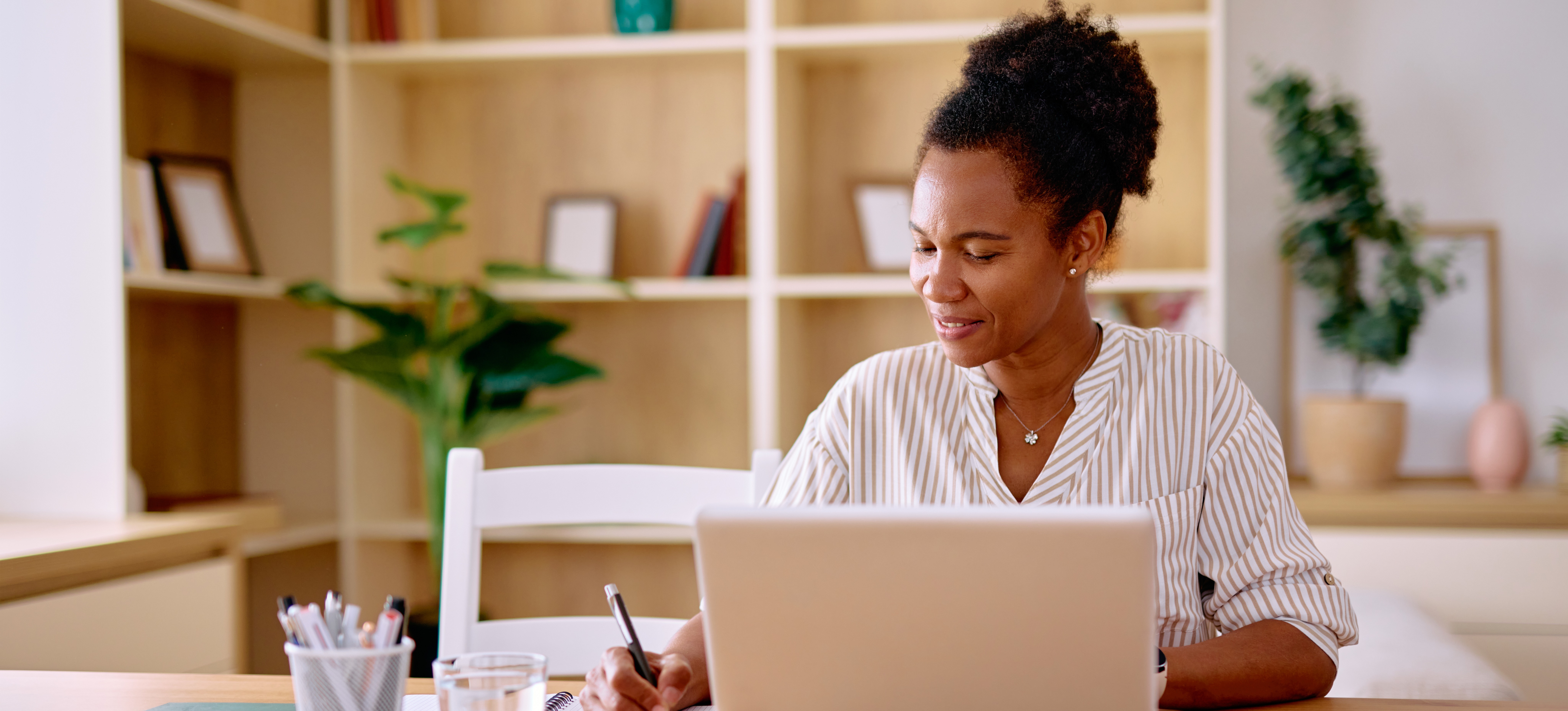[Featured Image] A professional sits at a laptop in their home office using an adaptive learning program and writes notes on paper.
