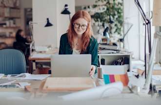 [Featured Image] A woman in glasses searches online for entry-level graphic design jobs on a laptop.