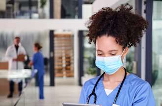 [Featured Image]: A legal nurse consultant, wearing a blue uniform and face covering, is looking at charts.