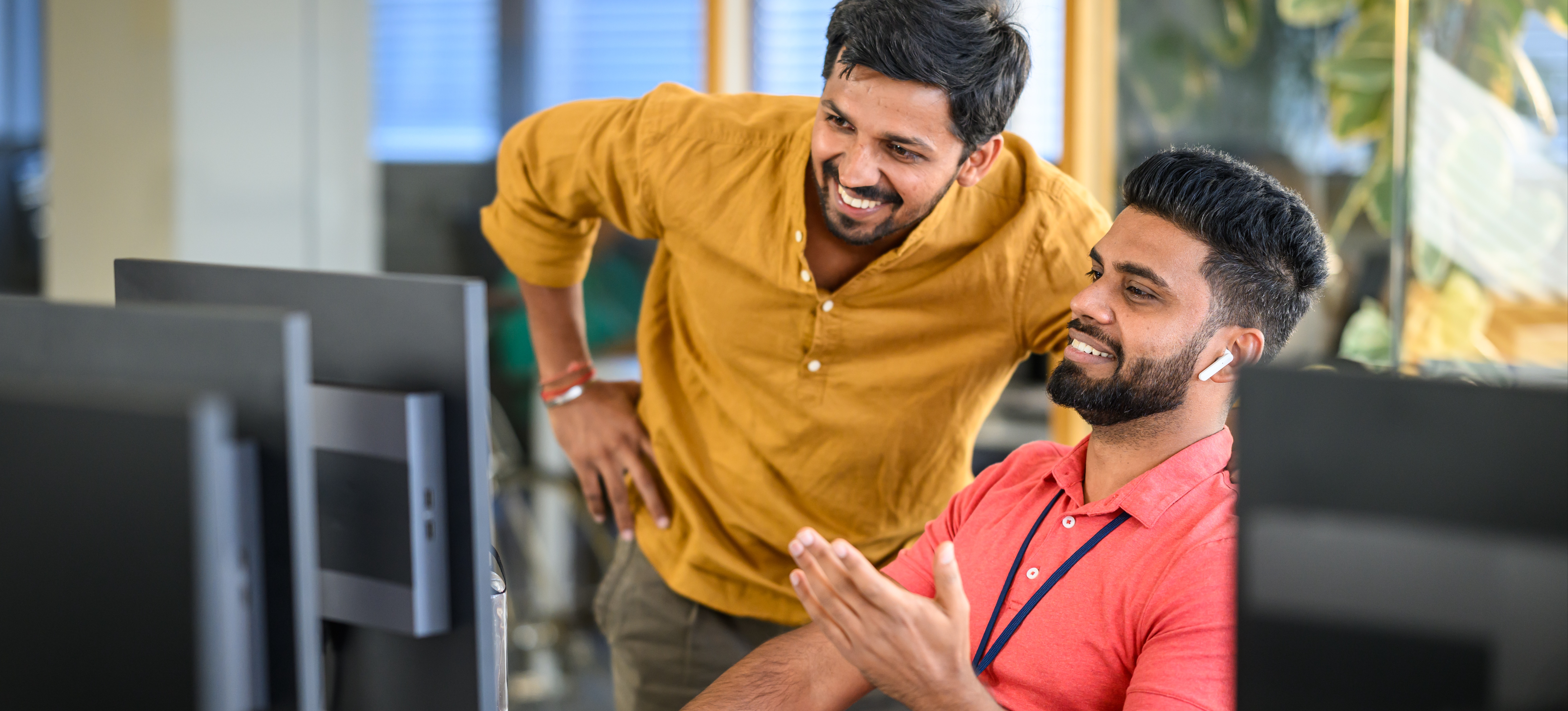 [Featured Image] A data analyst and a data scientist smile as they talk about the information they're looking at on a computer screen.