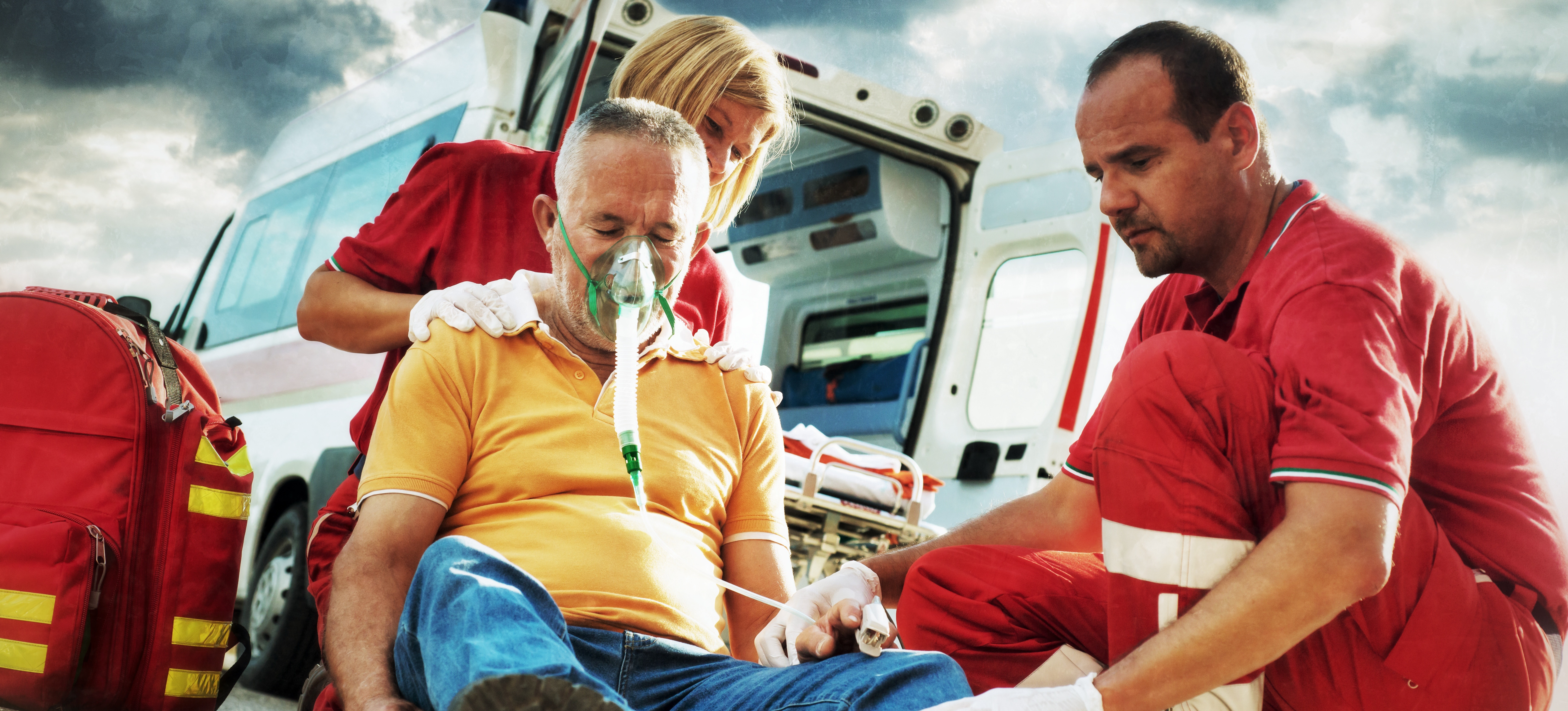 [Featured Image]: Two paramedics assist a person on the side of the road. If you're curious about this life-saving work, find out how long it takes to become a paramedic.
