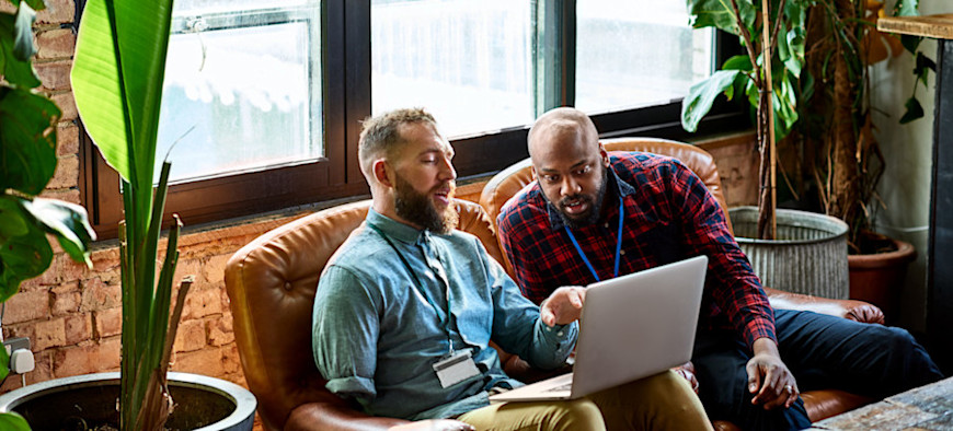 [Featured Image] Two work colleagues use a laptop to analyze work related bayesian statistics
