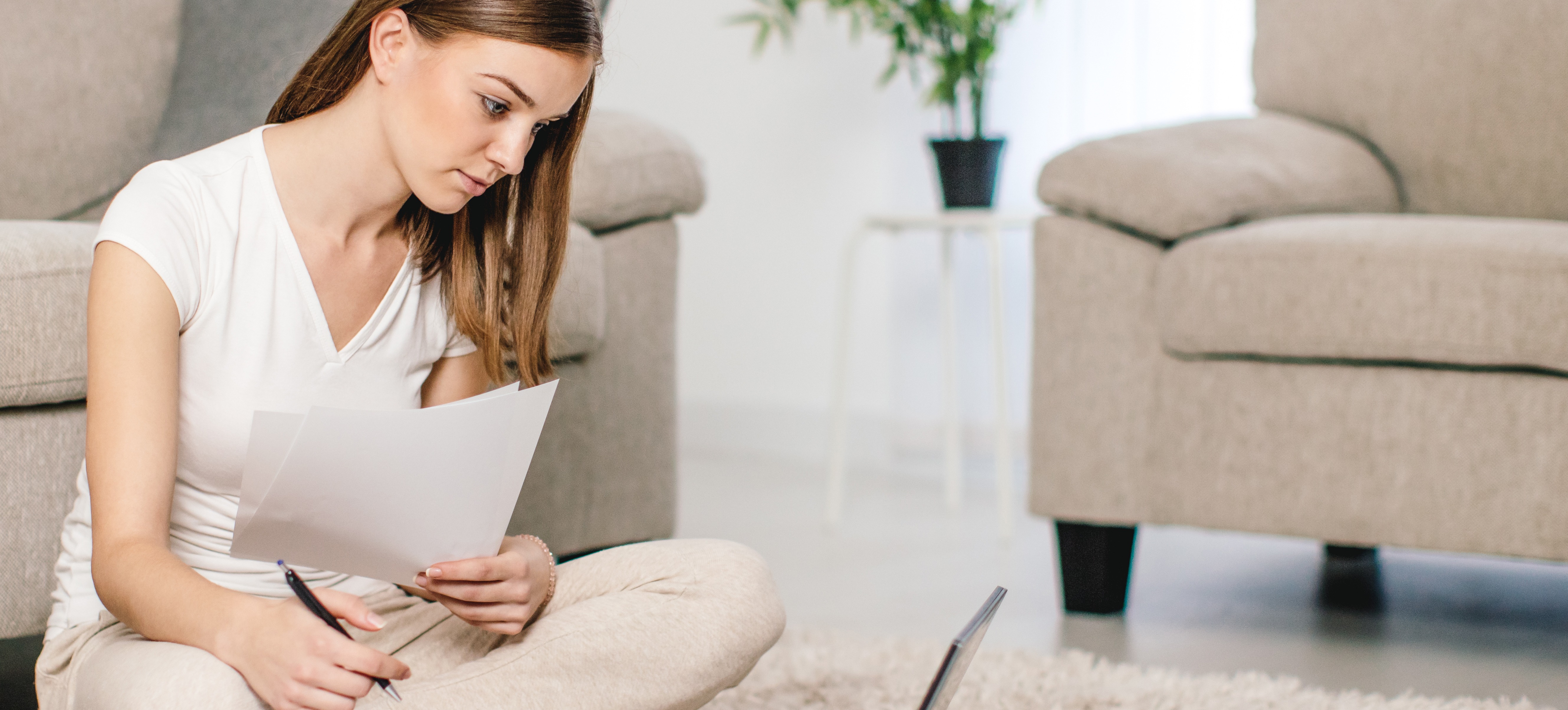 [Featured Image] A woman sits on the floor at home with her laptop and a pen and paper while studying to earn her real estate license, one of many popular non-degree programs.
