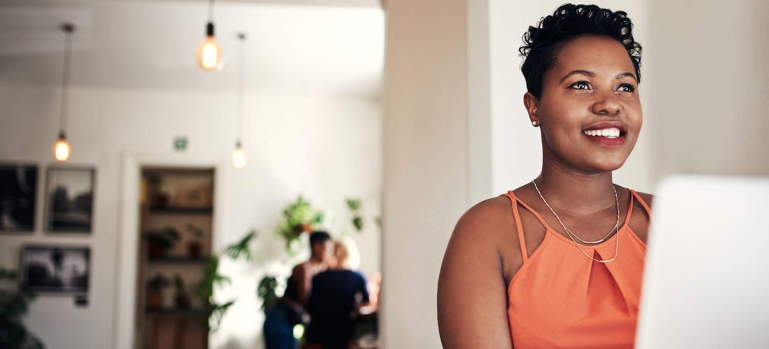 [Featured image] A person smiles off into the distance while sitting in front of their laptop.