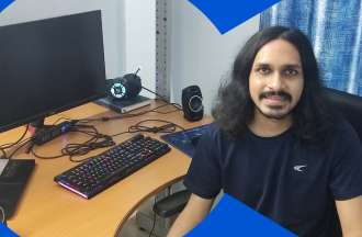 [Featured image] Web developer and CU Boulder MS in Data Science student Kaushik Muthyalu poses in front of his computer setup at home.