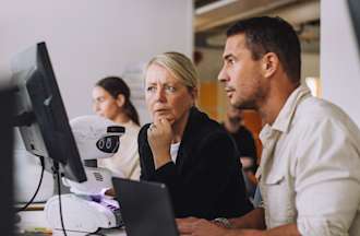 [Featured image] Two front-end developers are working together while looking at a desktop. 