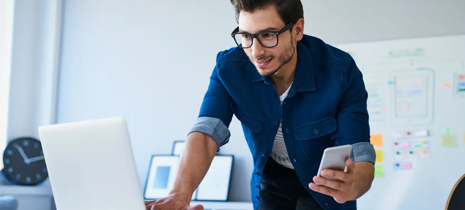 [Featured image] An Android app developer in a blue shirt works with a laptop and a smartphone. 