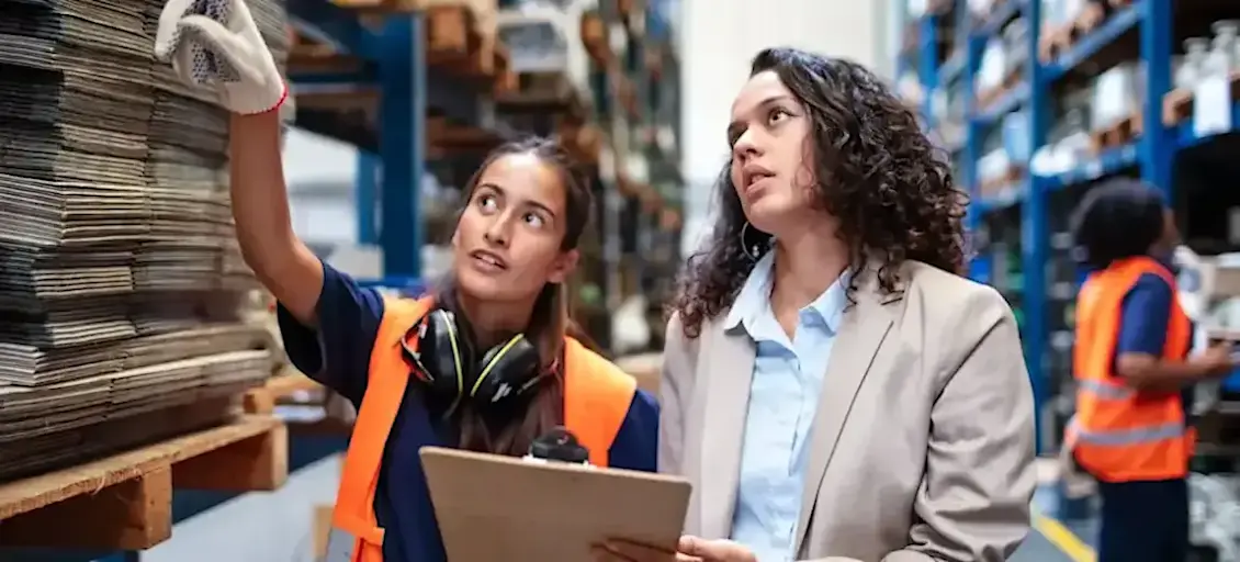 [Featured Image] A product manager and project manager are at a material supplier discussing what they need; one person is holding a clipboard while the other is pointing to materials. 