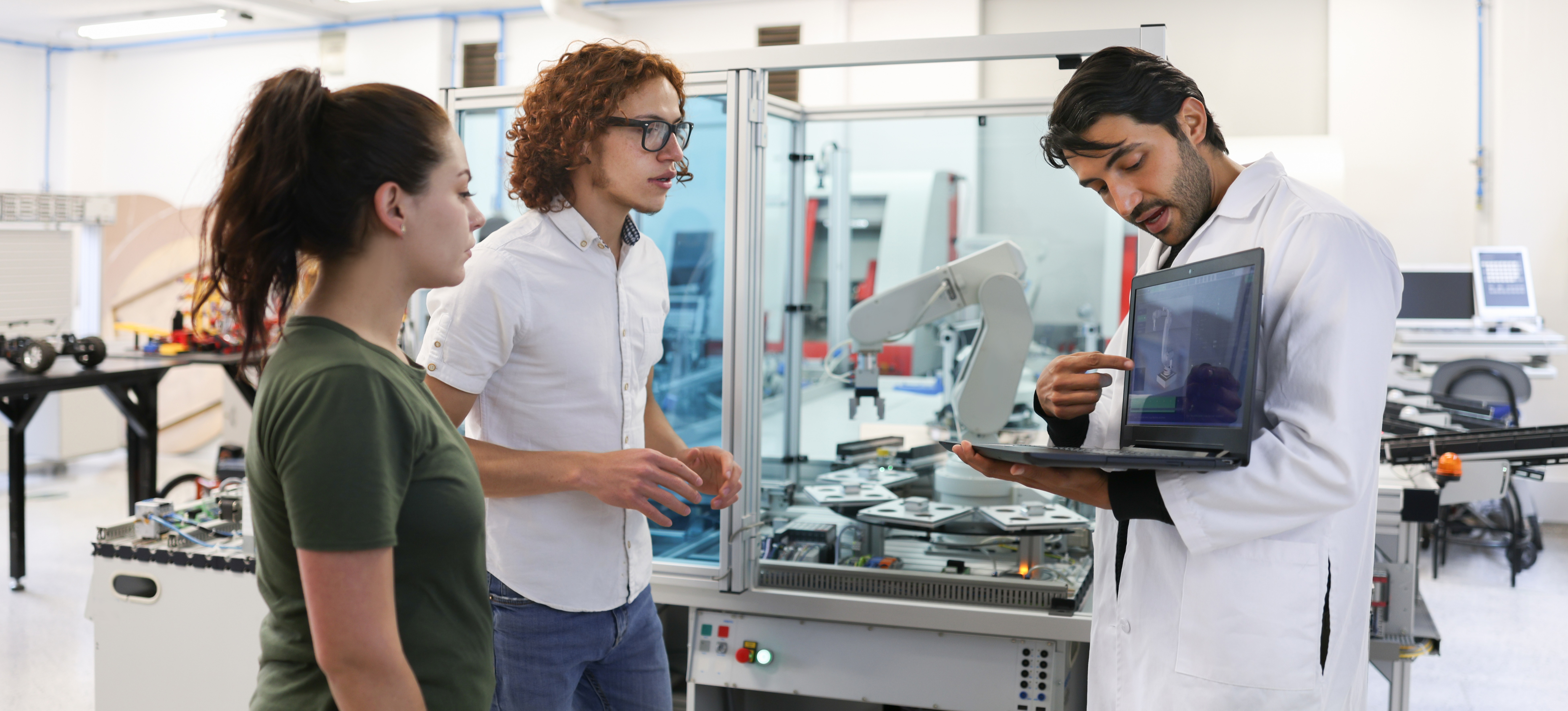 [Featured Image] A teacher in an engineering lab is showing two students how AI can help them make money.
