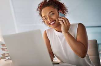 [Featured Image] An employee uses a laptop while using a phone.  