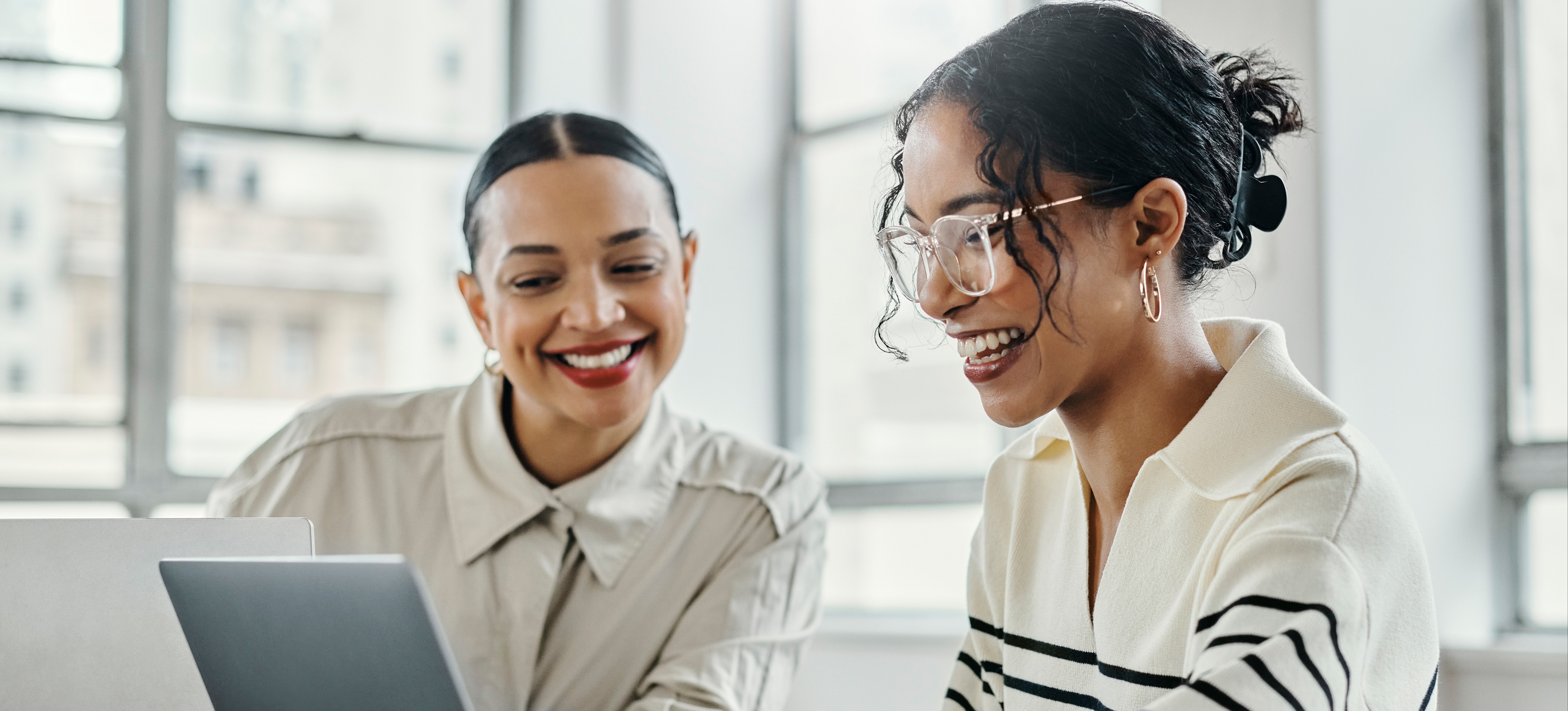 [FEATURED IMAGE] An HR analyst wearing glasses works at their laptop computer with a colleague. 
