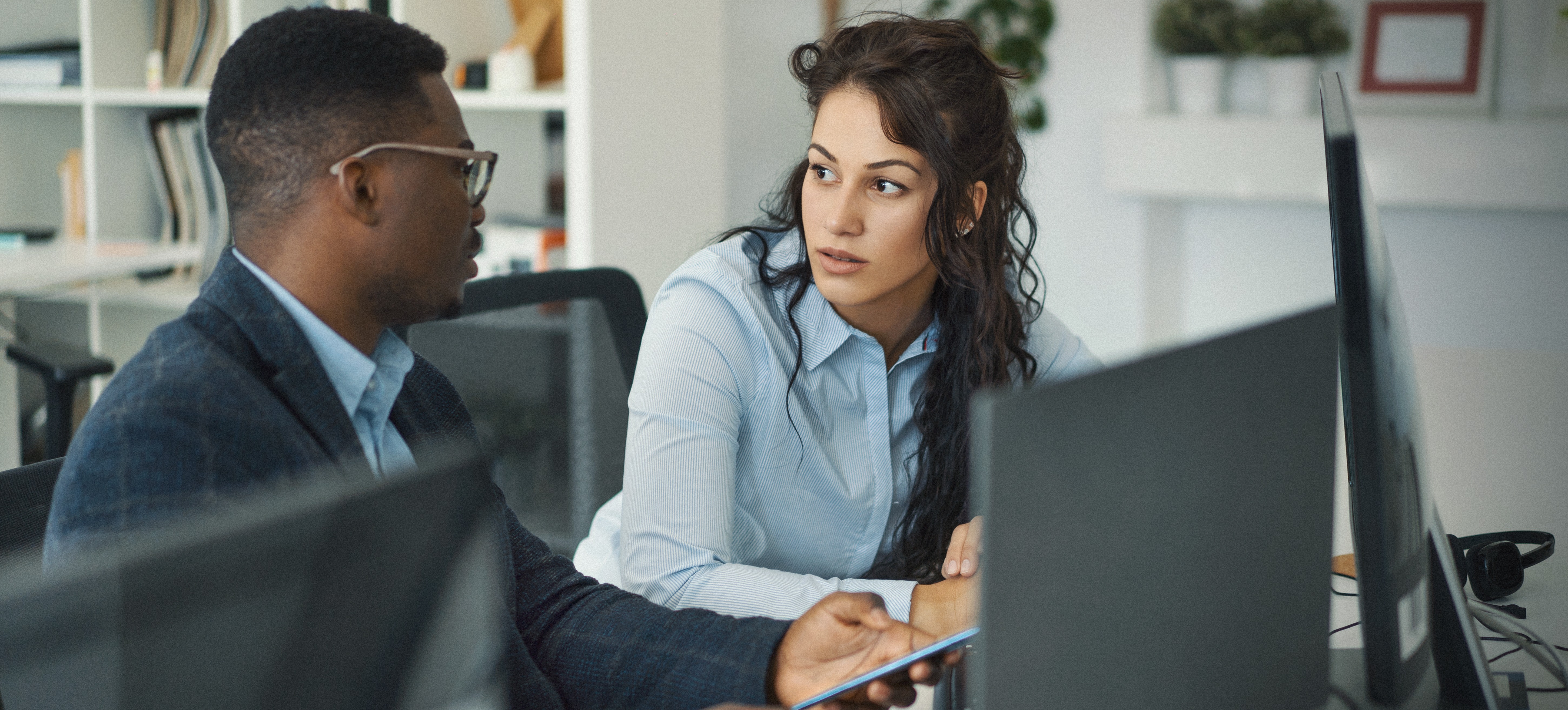 [Featured Image] Two colleagues sit at their computer screens and discuss word embedding in NLP.
