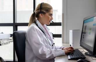 [Featured Image] A woman in a medical office sits at a desktop computer and types.