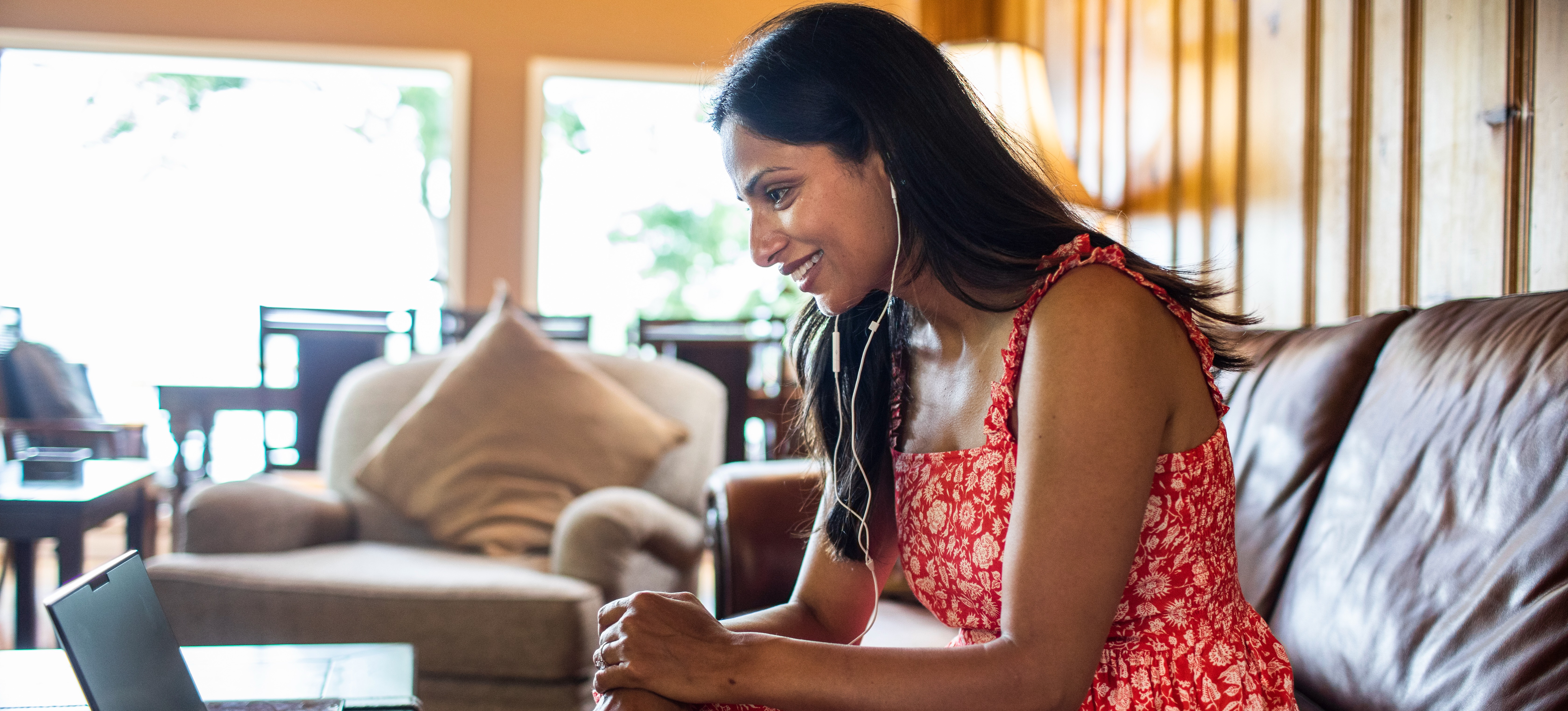 [Featured Image] A woman sits in her home with a laptop and earbuds and studies for the PTE exam. 