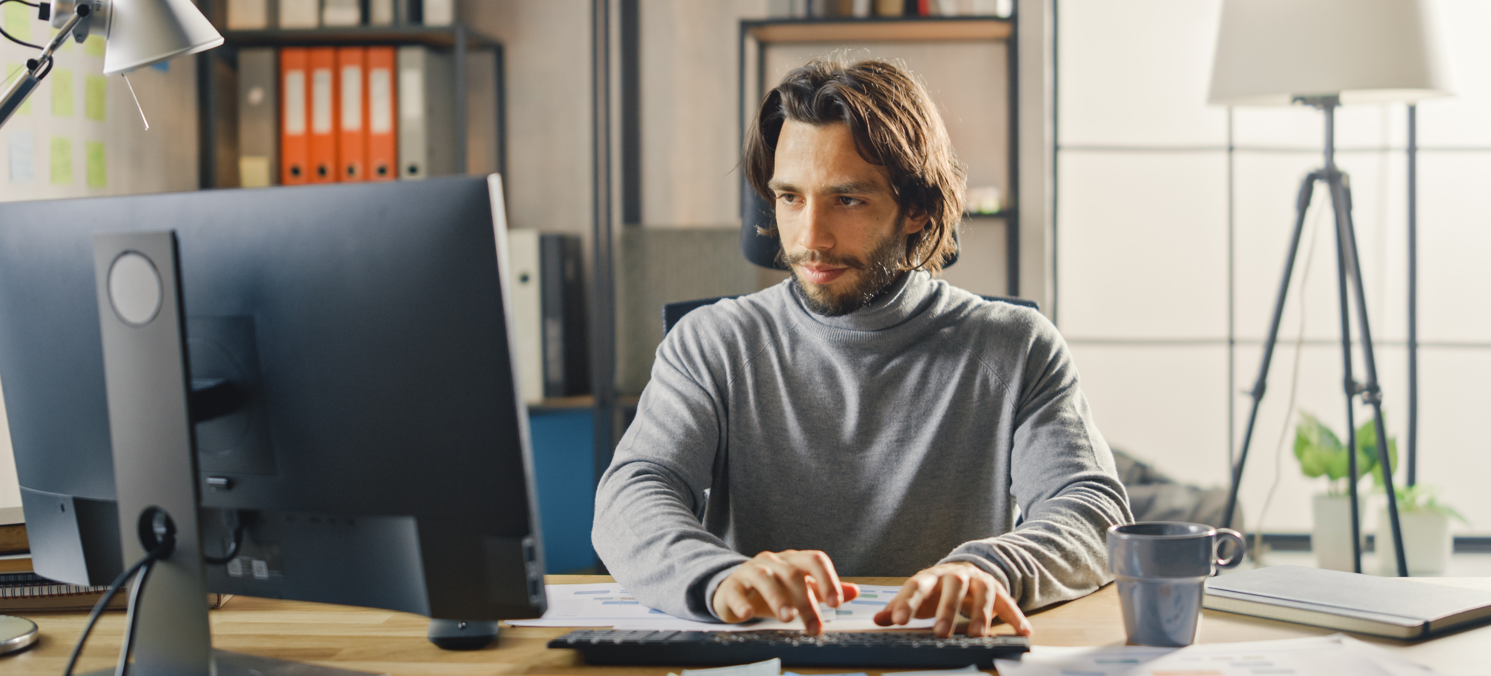 [Featured Image] An IT professional who earns an AWS cloud practitioner salary works at a computer in their home office.