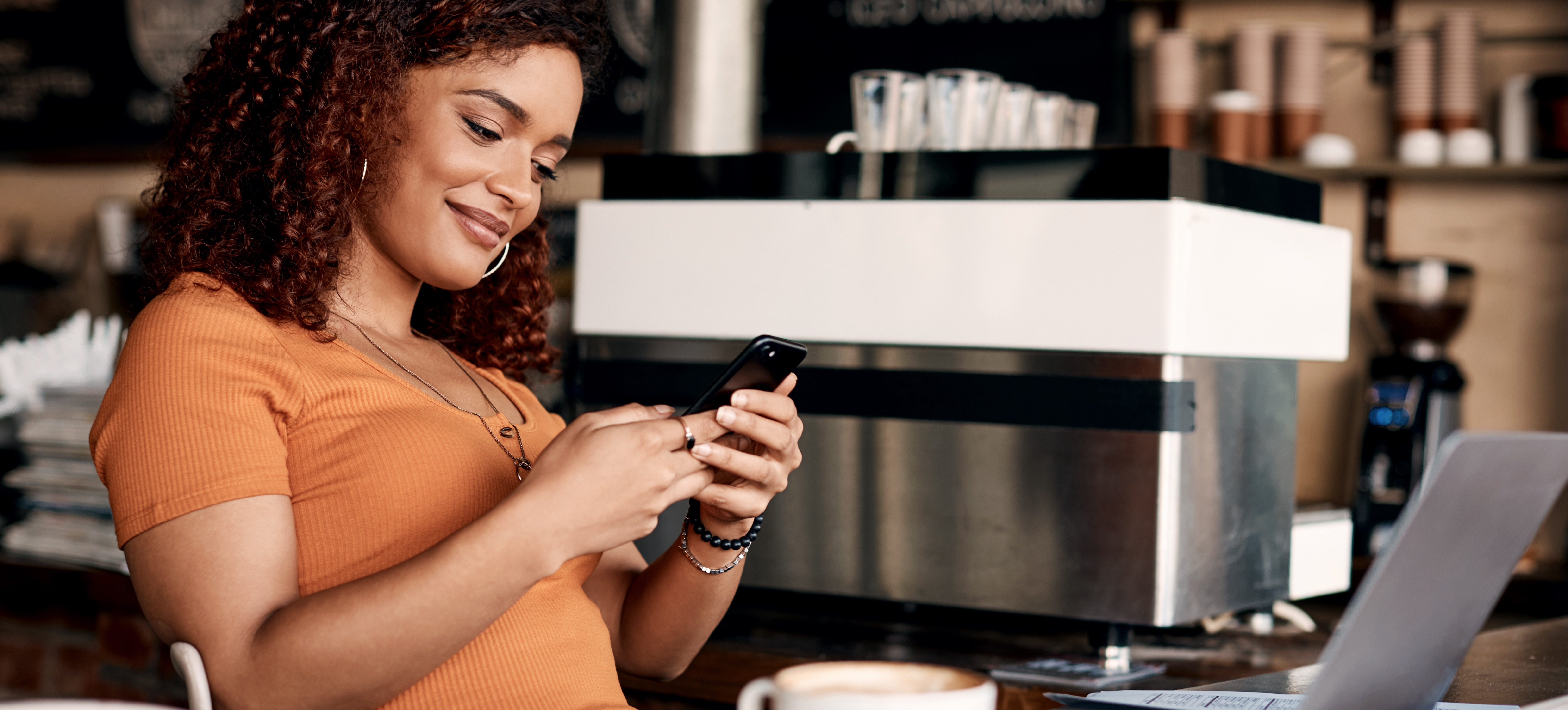 [Featured image] A smiling person in a coffee shop receives a push notification on their cell phone from a geofencing marketing strategy.