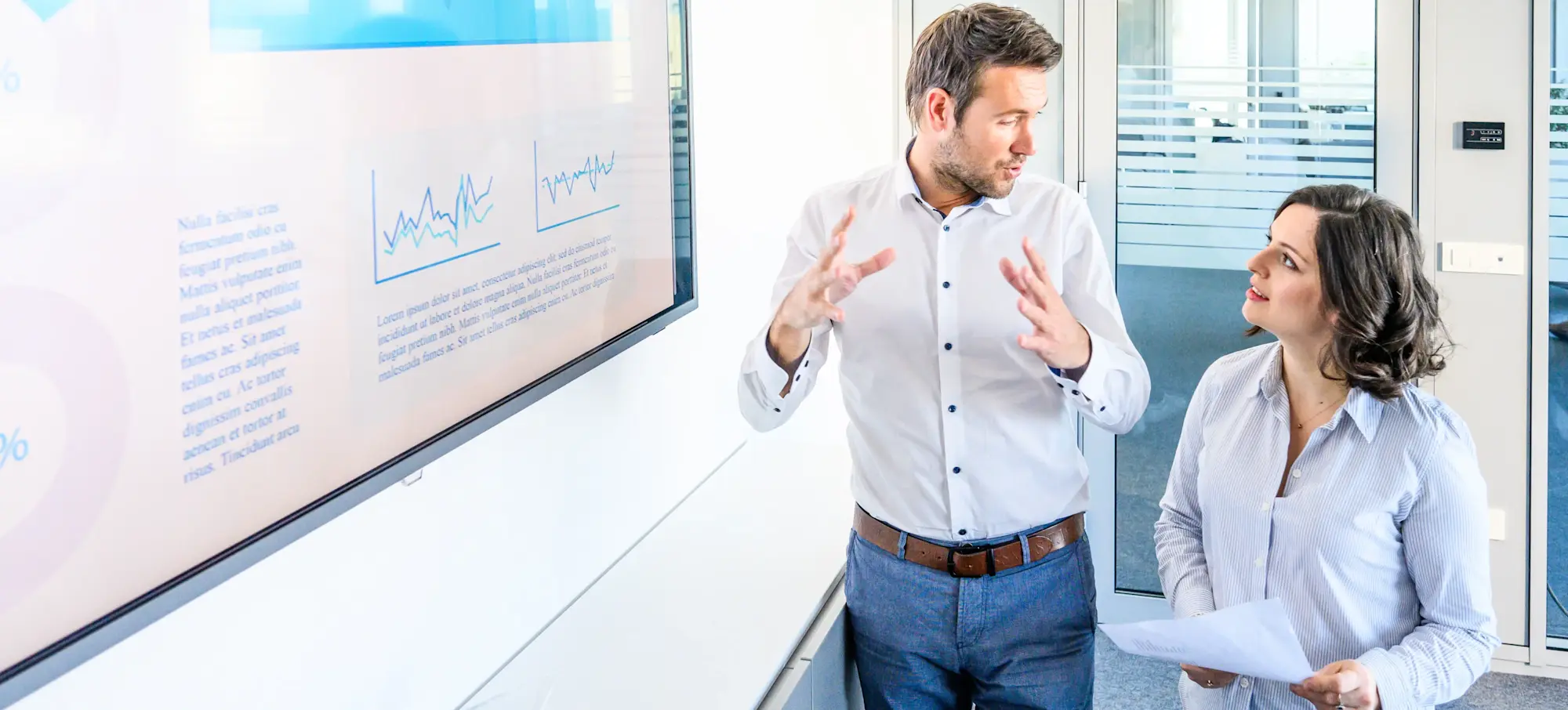 [Featured Image] A male and female coworker stand in an office next to a presentation screen discussing overfitting in their business.
