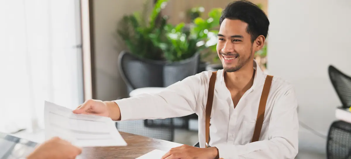 [Featured Image] A job applicant in an interview with a manager, handing over a MATLAB resume in a professional workplace setting.
