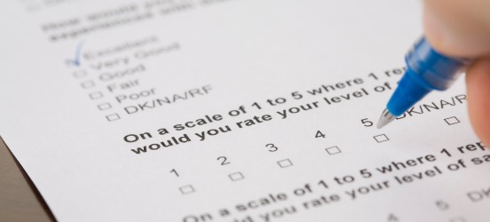[Featured image] Closeup of a hand holding a pen and marking answers on a statistical survey.