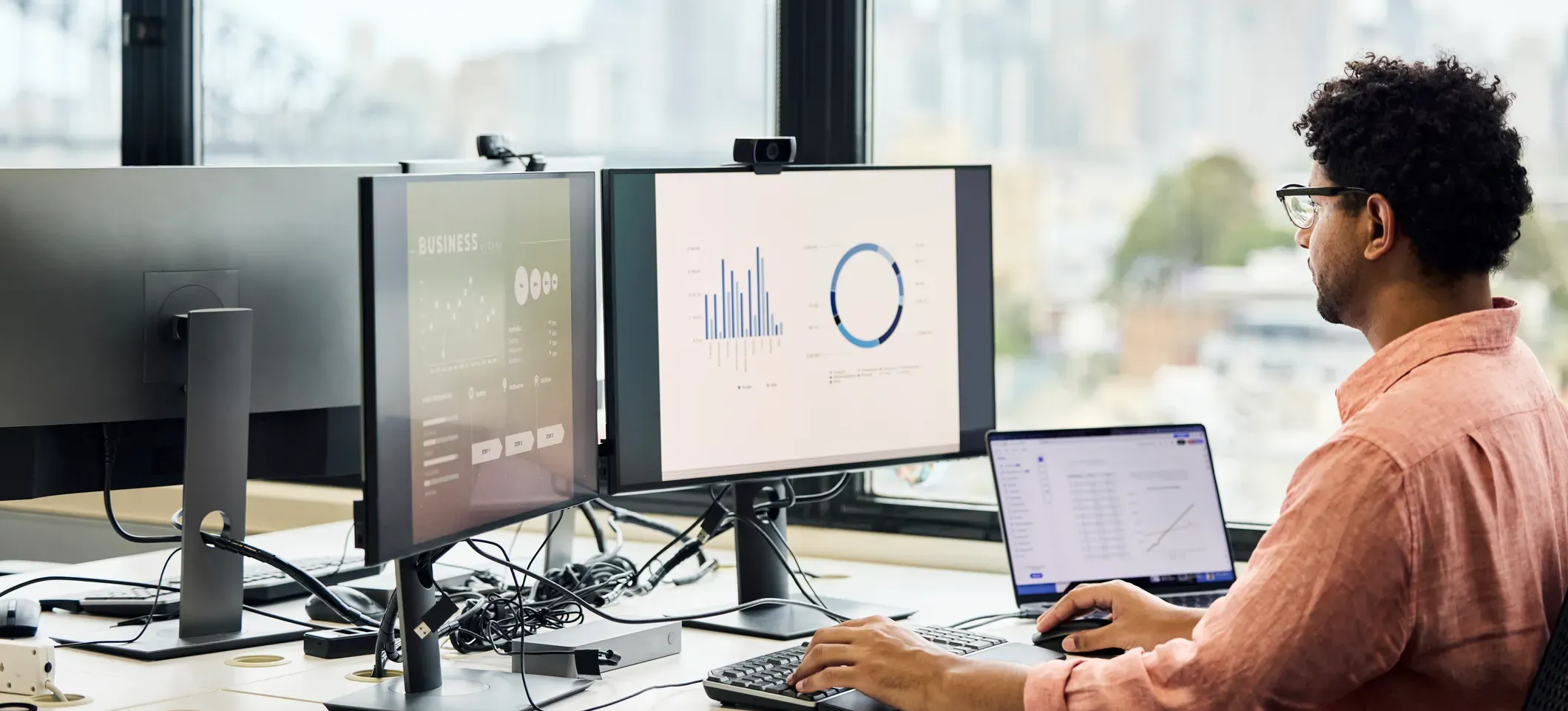 [Featured Image] A business professional works at their desk using several types of computers to accomplish their various tasks.
